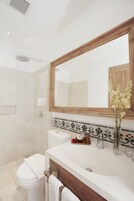 Une salle de bain avec des toilettes blanches, un lavabo avec un meuble-vasque en bois, un miroir et un espace douche.