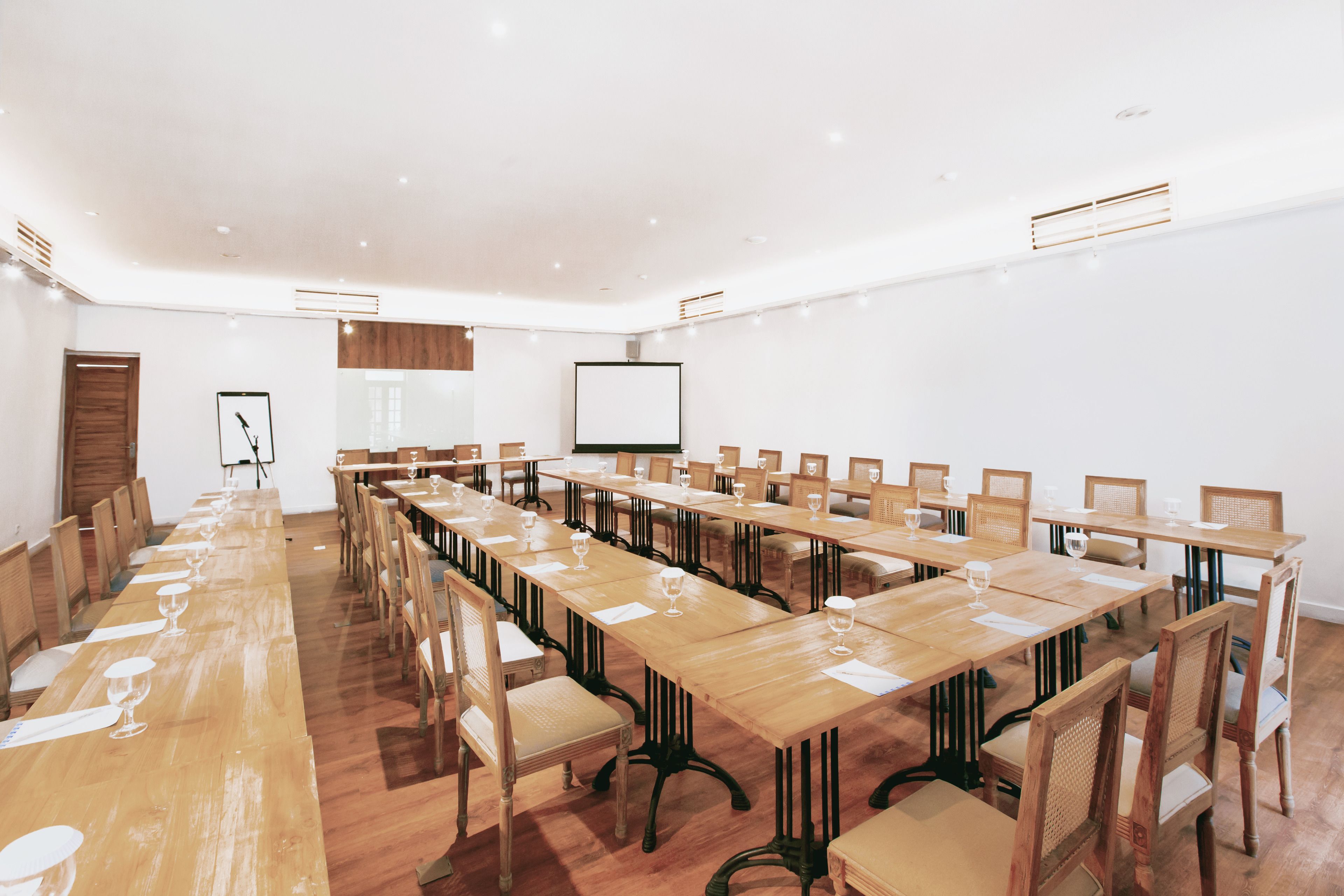 Une salle de conférence équipée de longues tables, de chaises et d’un écran de projection.