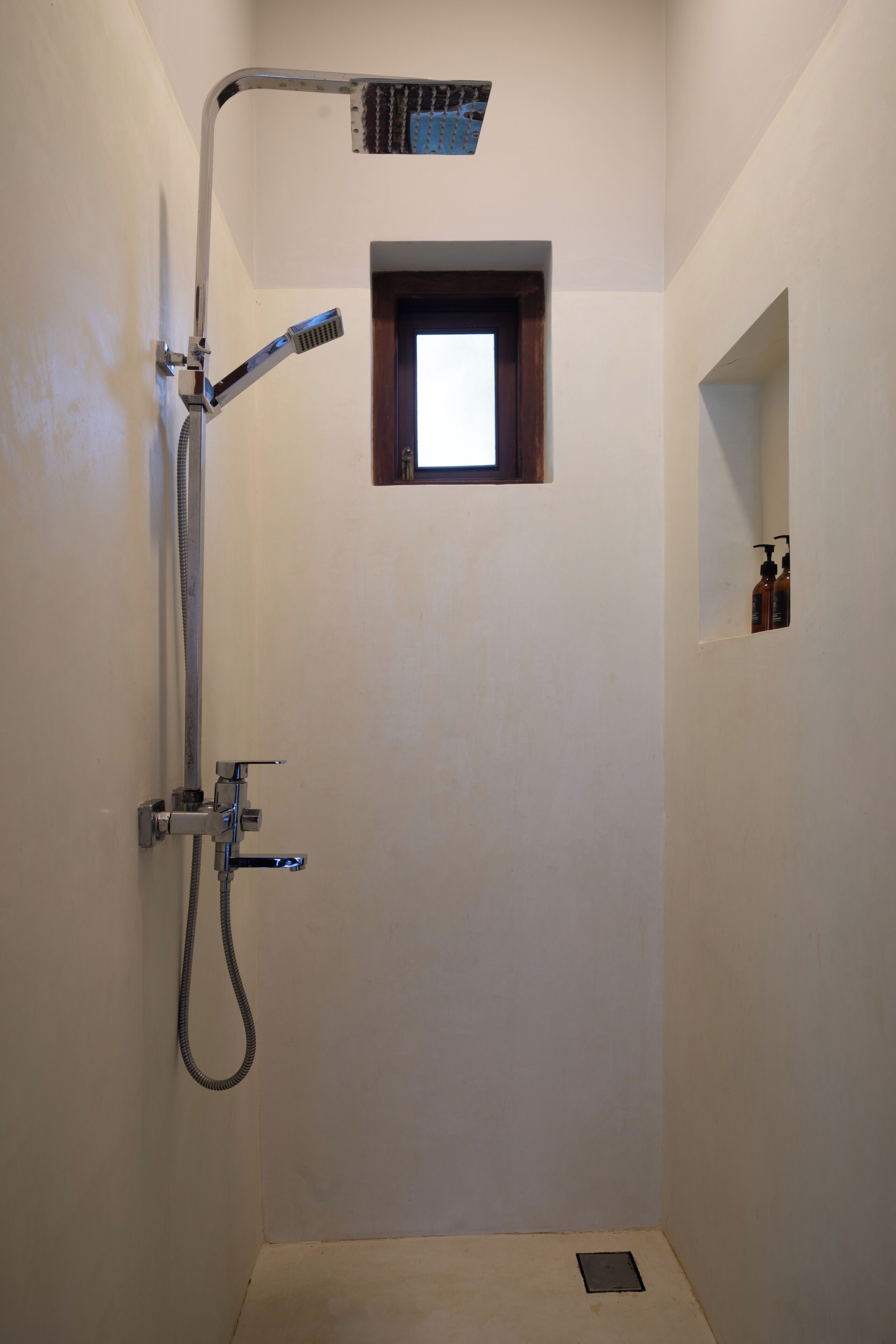 A shower with a handheld showerhead, a wall-mounted faucet, and a small window.