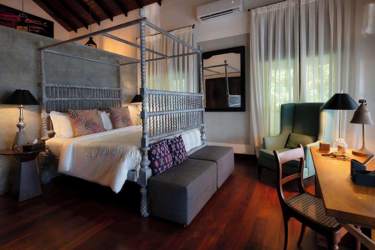 A four-poster bed with a bench, a dining table with chairs, and a green armchair.