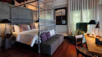 A four-poster bed with a bench, a dining table with chairs, and a green armchair.