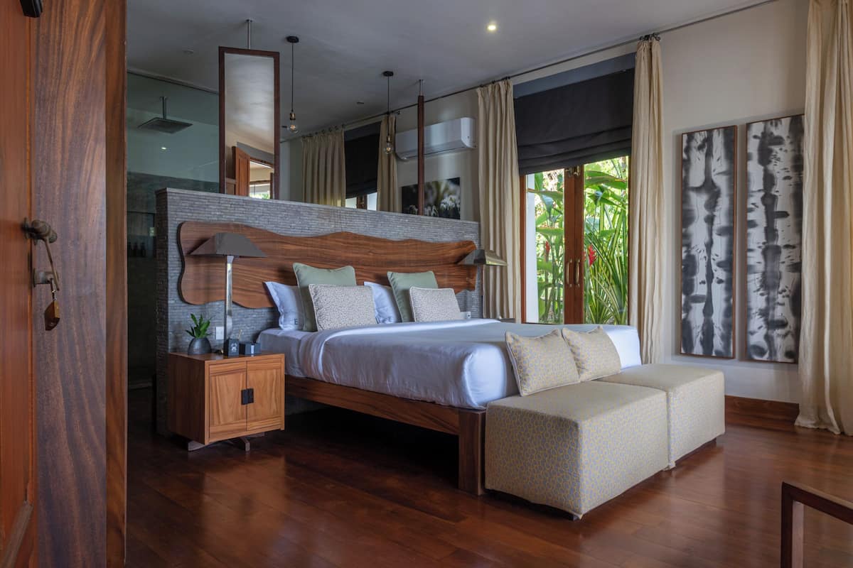 A modern bedroom with a wooden headboard, a large bed with multiple pillows, a bench, and a nightstand.