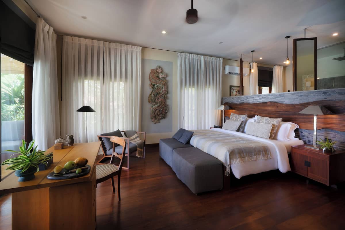 A modern bedroom with a large bed, bedside tables, a desk with a plant, and a view of the outdoors.