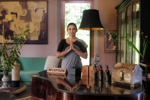 A reception desk with a sign reading 'RECEPTION' and 'BESESSION,' a lamp, a vase with plants, and a cabinet with books. - Eraeliya Villas & Gardens (Weligama)