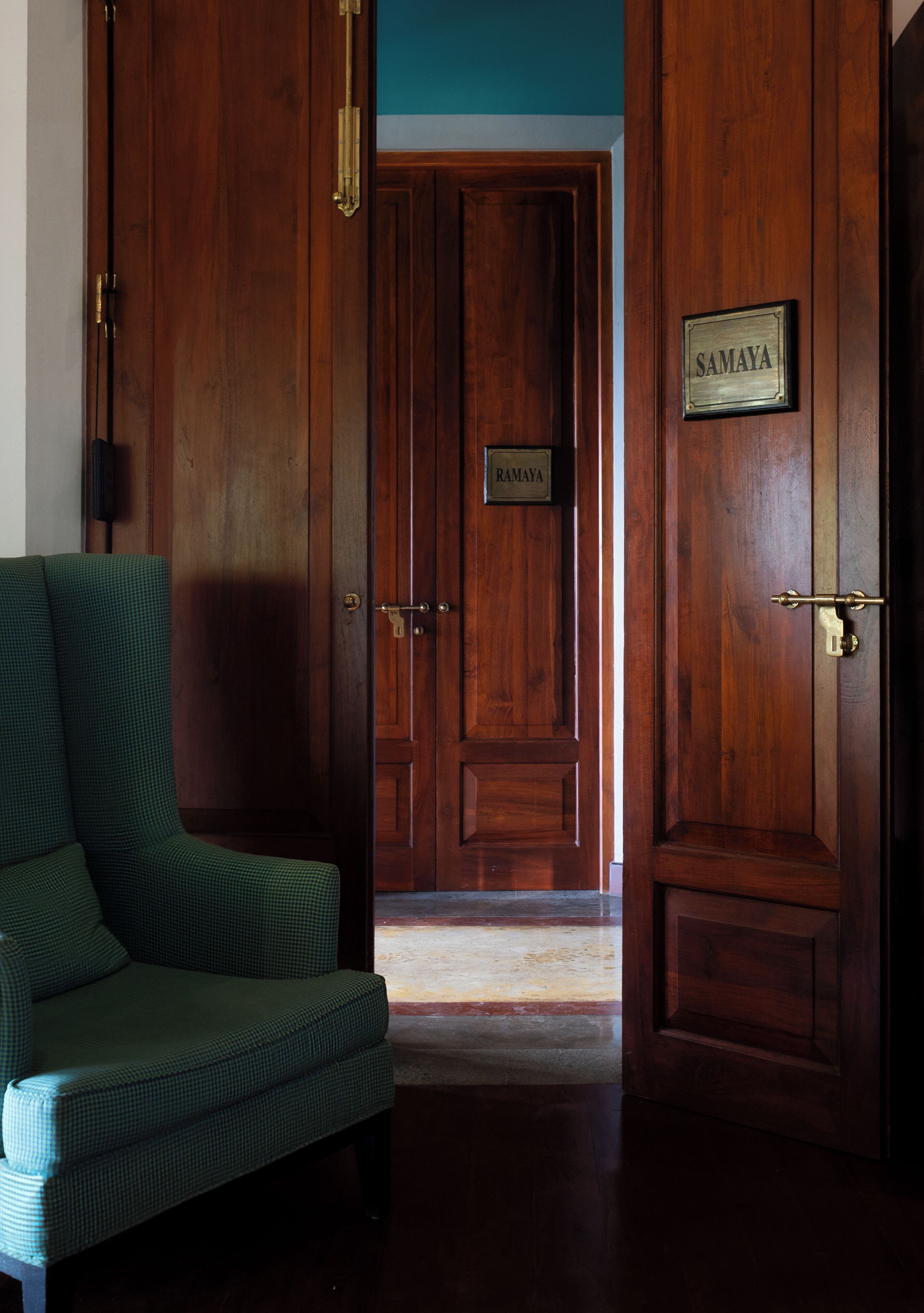 A wooden door with a brass nameplate reading 'SAMAYA' and a green upholstered chair.