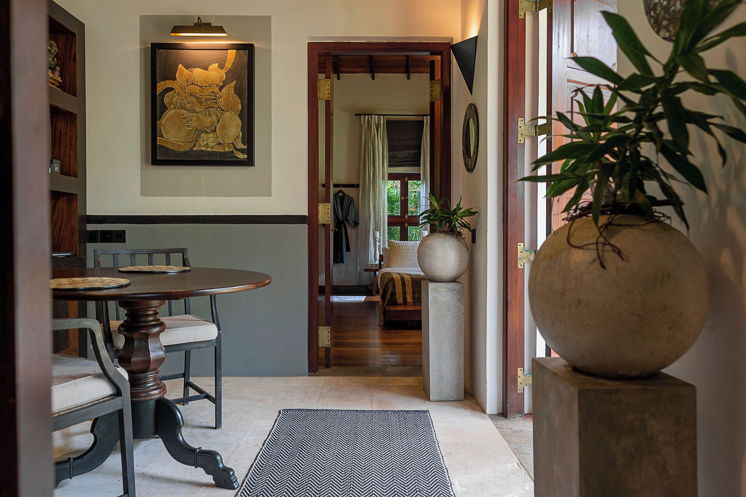 A dining area with a wooden table and chairs, a large vase, and a framed artwork on the wall.