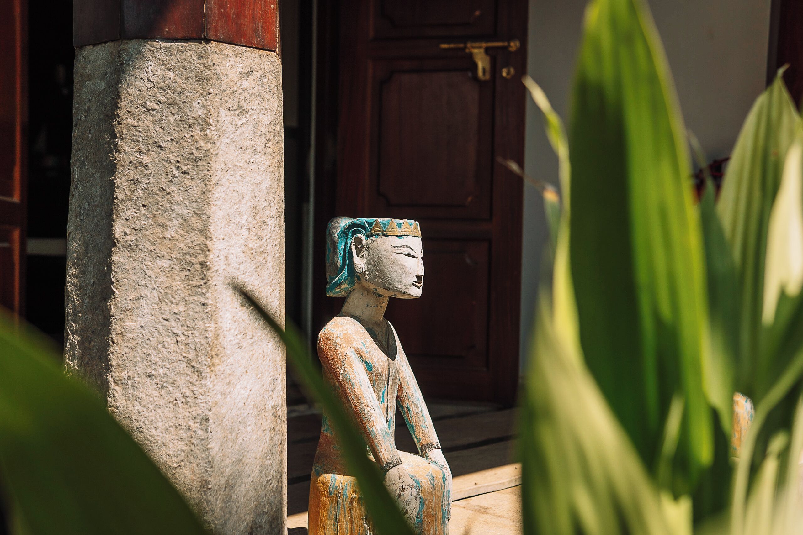 A statue of a seated figure with a head covering, positioned against a building's corner.