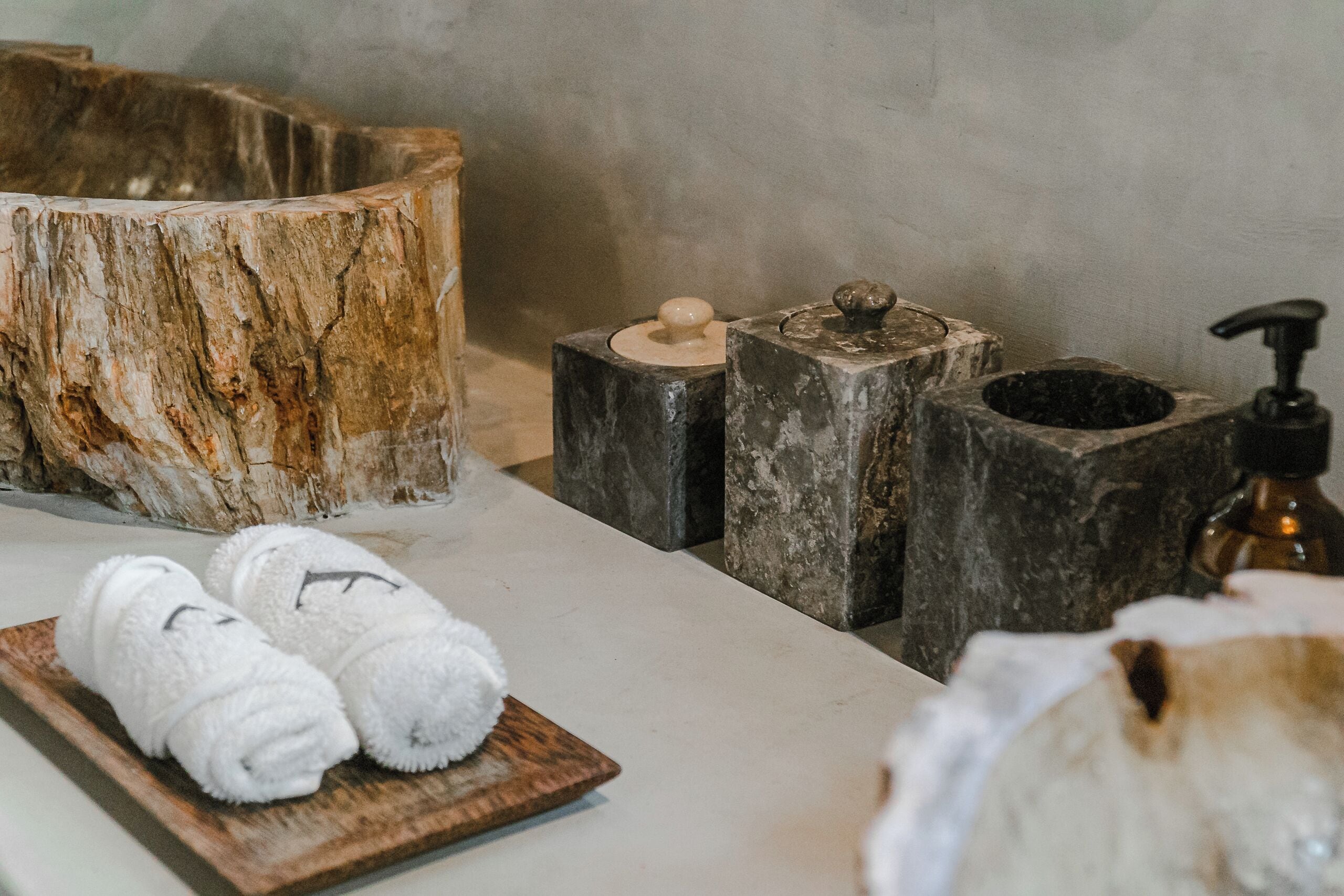 A wooden bowl, a wooden tray with towels, a soap dispenser, and a stone-like container.