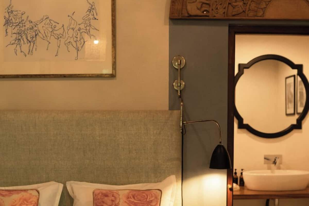 A hotel room with a bed, a framed artwork, a nightstand, a lamp, a bathroom with a sink and mirror.