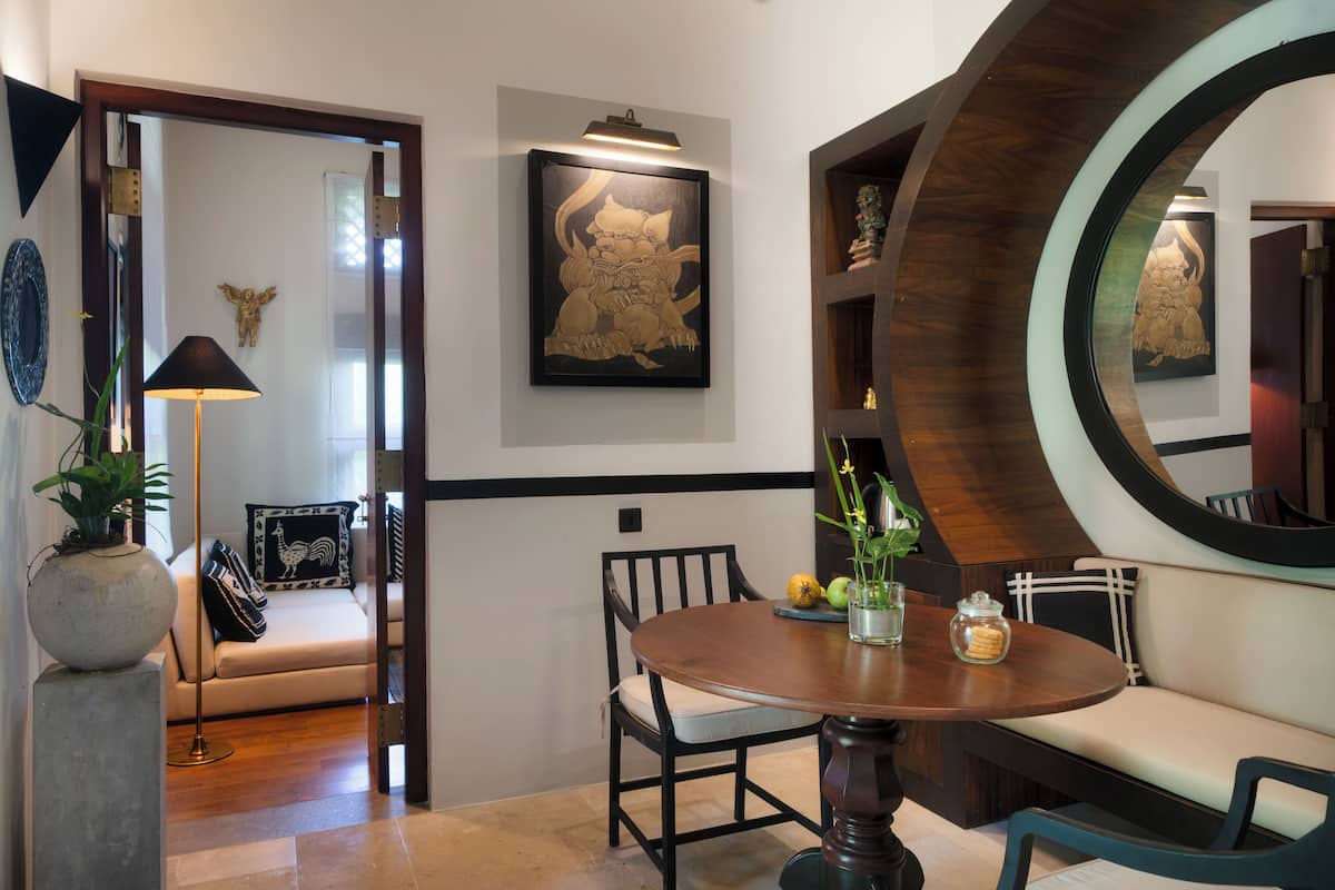 A dining area with a round table, chairs, and a bench. There is a wall-mounted artwork and a decorative mirror.