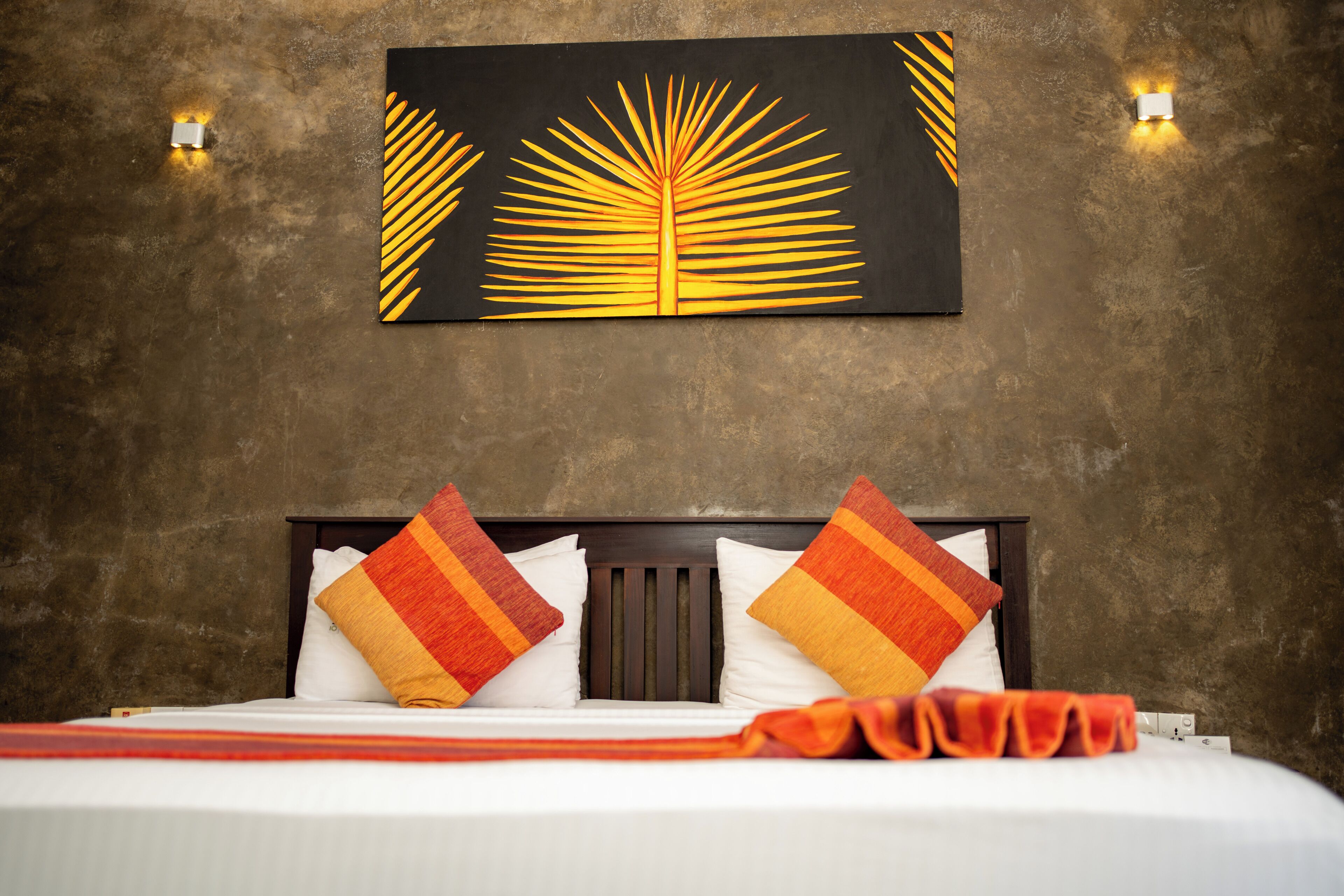 A hotel room with a bed, two pillows, a blanket, and a wall-mounted artwork.