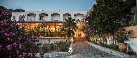 A courtyard with a stone pathway leading to a building with multiple balconies. There are potted plants and flowers along the pathway.