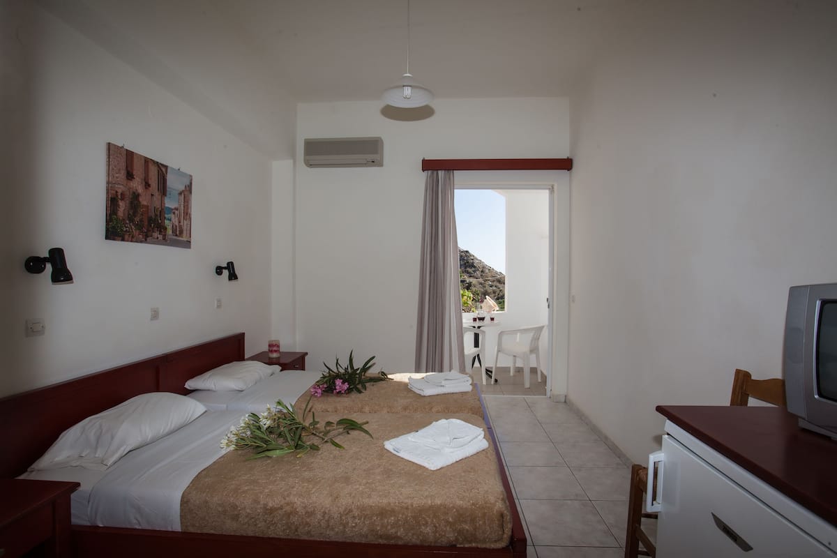 A hotel room with a bed, a desk, a chair, a television, and a balcony with a view of the landscape.