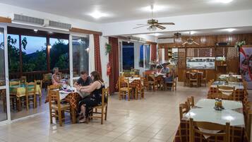 Un restaurante con varias áreas de comedor, ventanas amplias y una cocina visible a través de un umbral abierto.