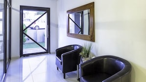 A reception area with a glass door, two black leather chairs, a potted plant, and a wooden-framed mirror on the wall. - Discovery Guest House (Windhoek)