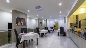 A modern dining area with tables set for service, a kitchen counter with appliances, and a clean, tiled floor. - Discovery Guest House (Windhoek)