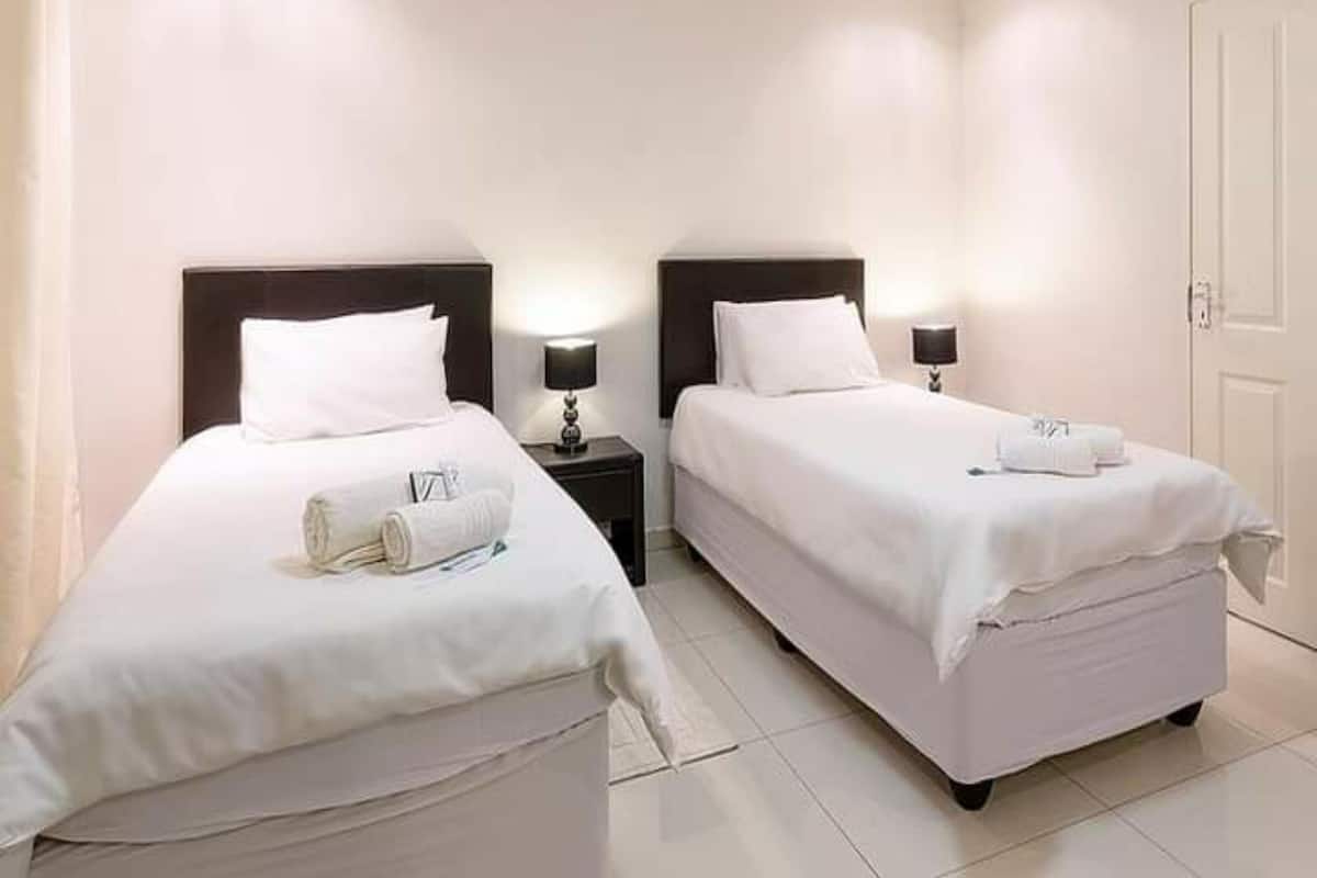 A hotel room with two beds, each with white linens and pillows, a nightstand with a lamp, and a door.