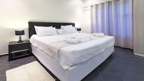 A neatly made bed with white linens, a bedside table with a lamp, and a large window with curtains. - Discovery Guest House (Windhoek)