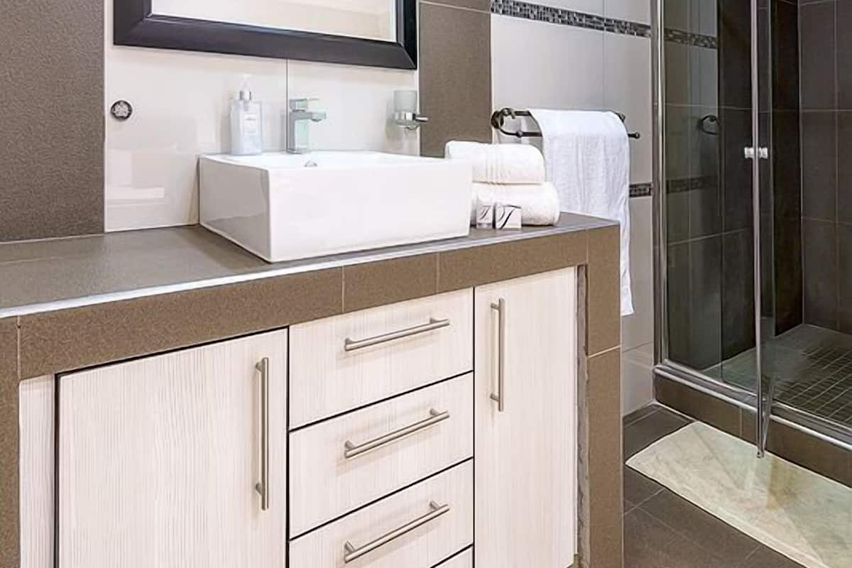 A modern bathroom with a large mirror, white sink, and a glass shower enclosure.