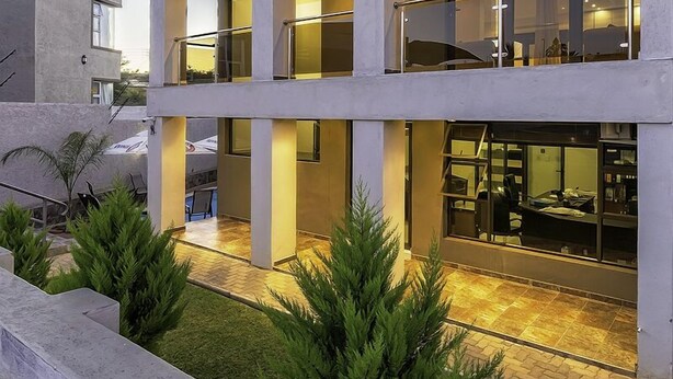 A modern building with a courtyard, featuring a glass facade, outdoor seating, and greenery. - Discovery Guest House (Windhoek)