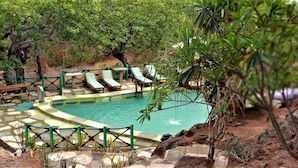 Zona de piscina amb gandules i una banca de fusta, envoltada de vegetació i un mur de pedra.