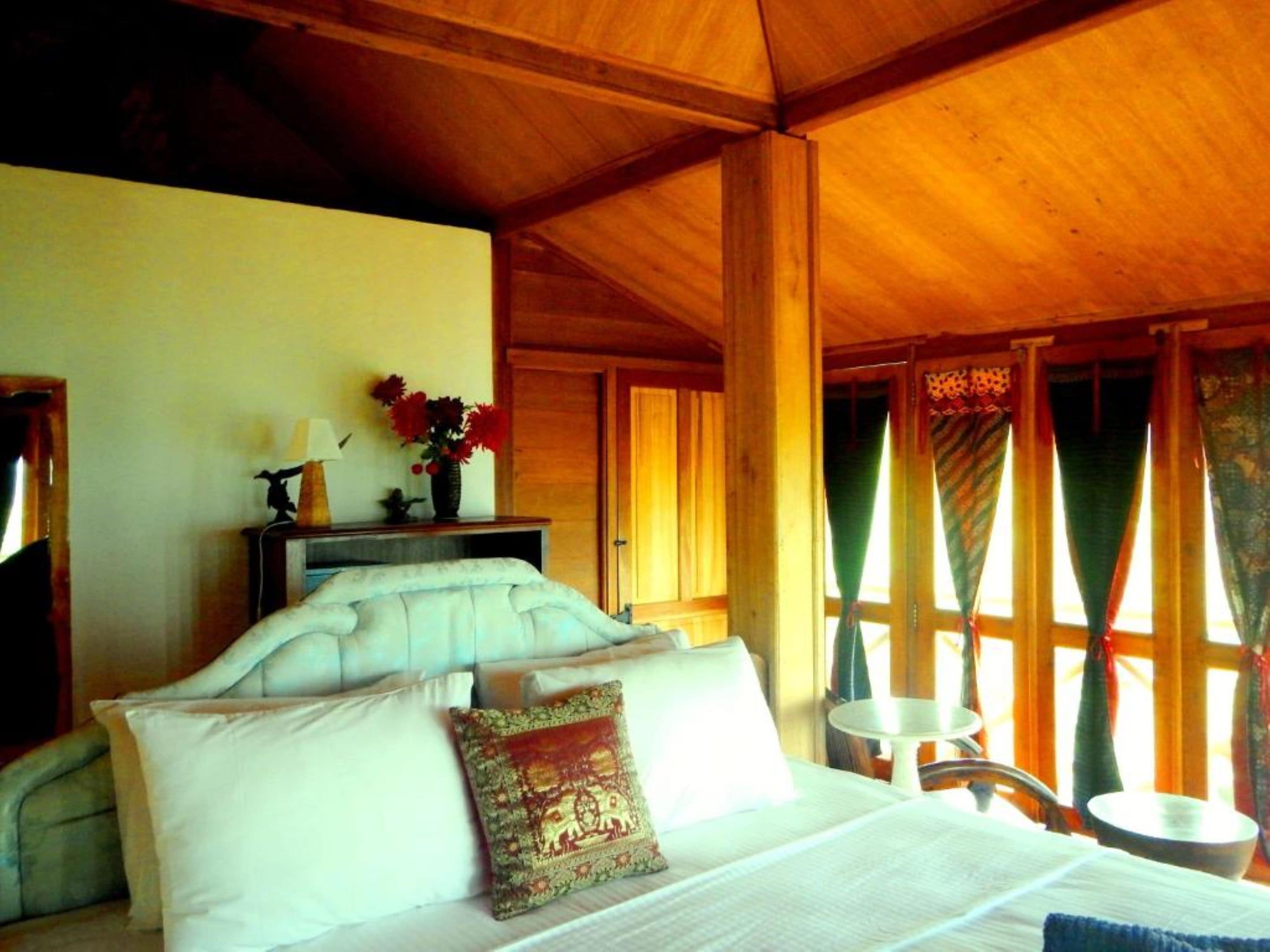 A wooden room with a bed, a small table, and a window with curtains.