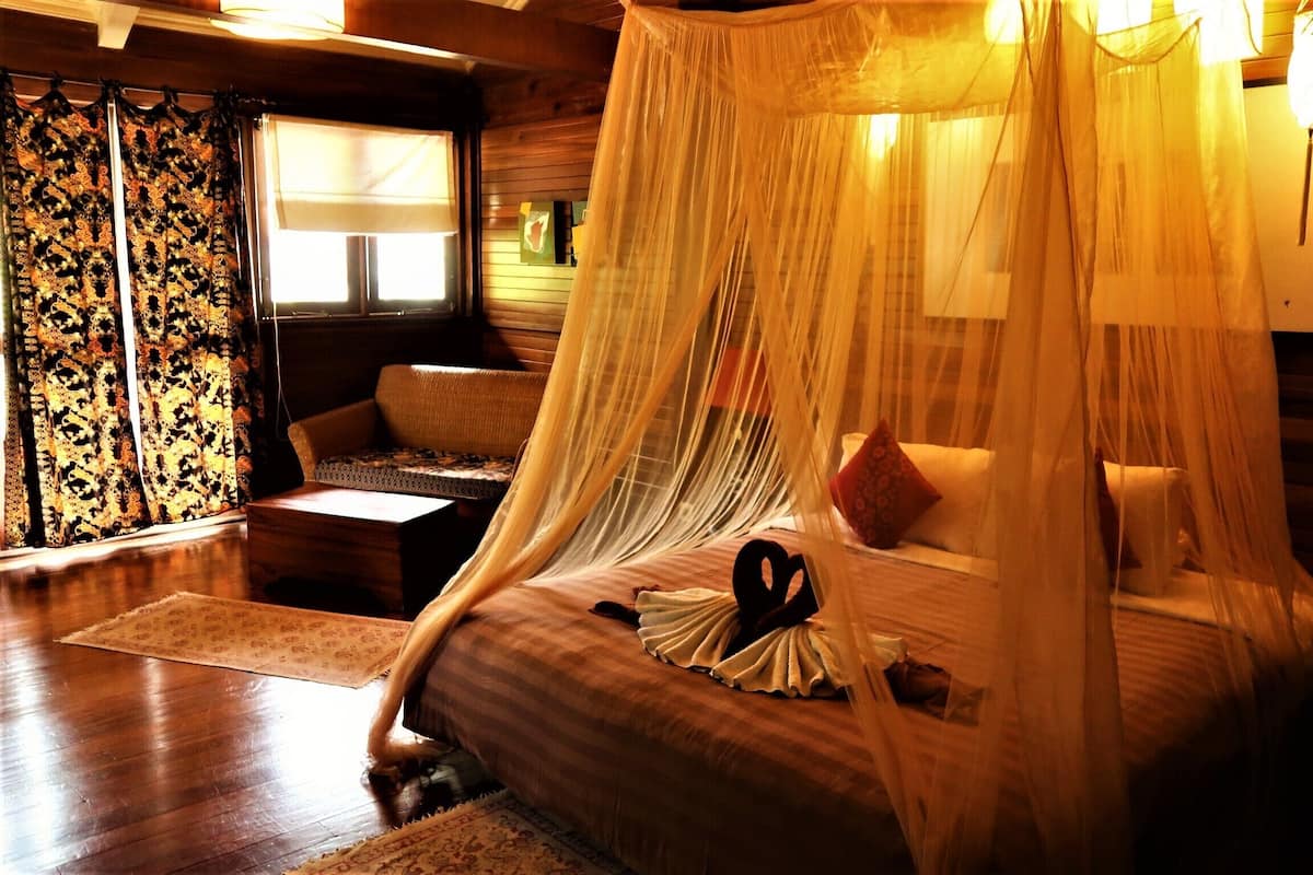 Una habitación con una cama bajo un dosel, un sofá, una mesita y una ventana con cortinas.