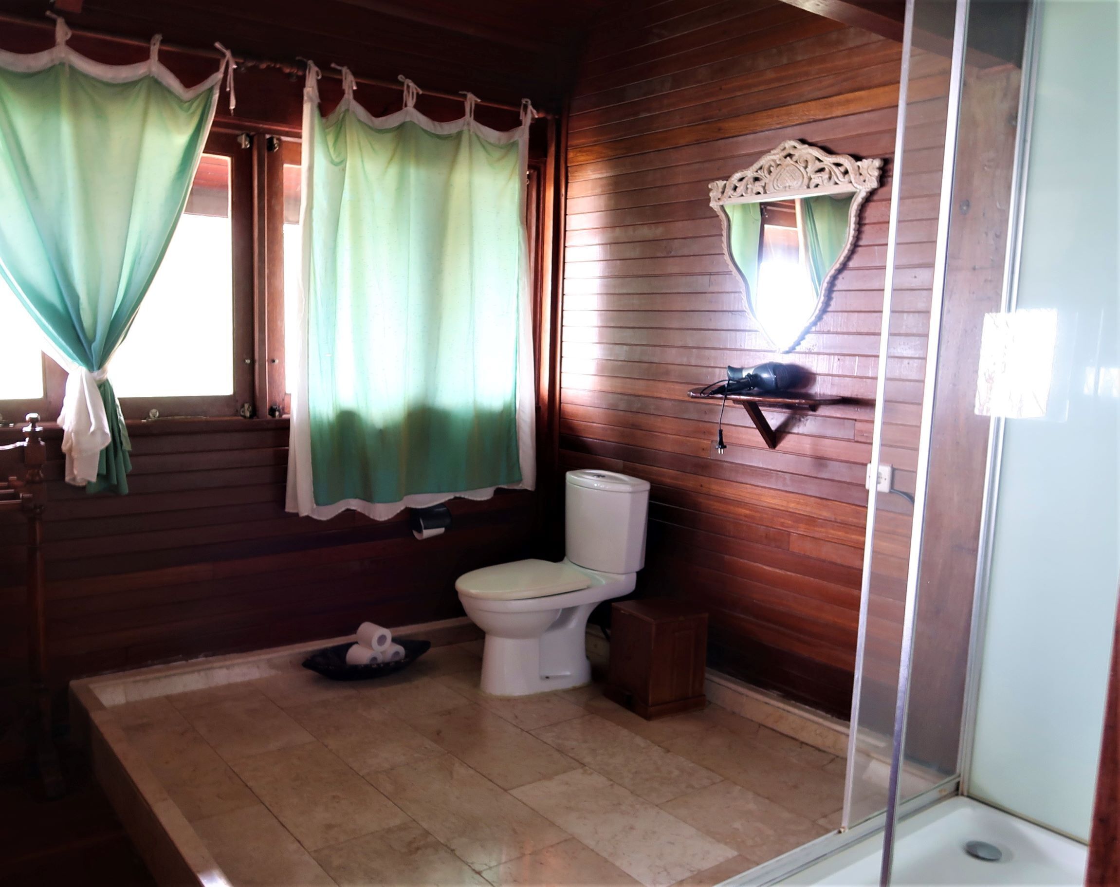 A bathroom with wooden walls, a toilet, a shower, and a sink.