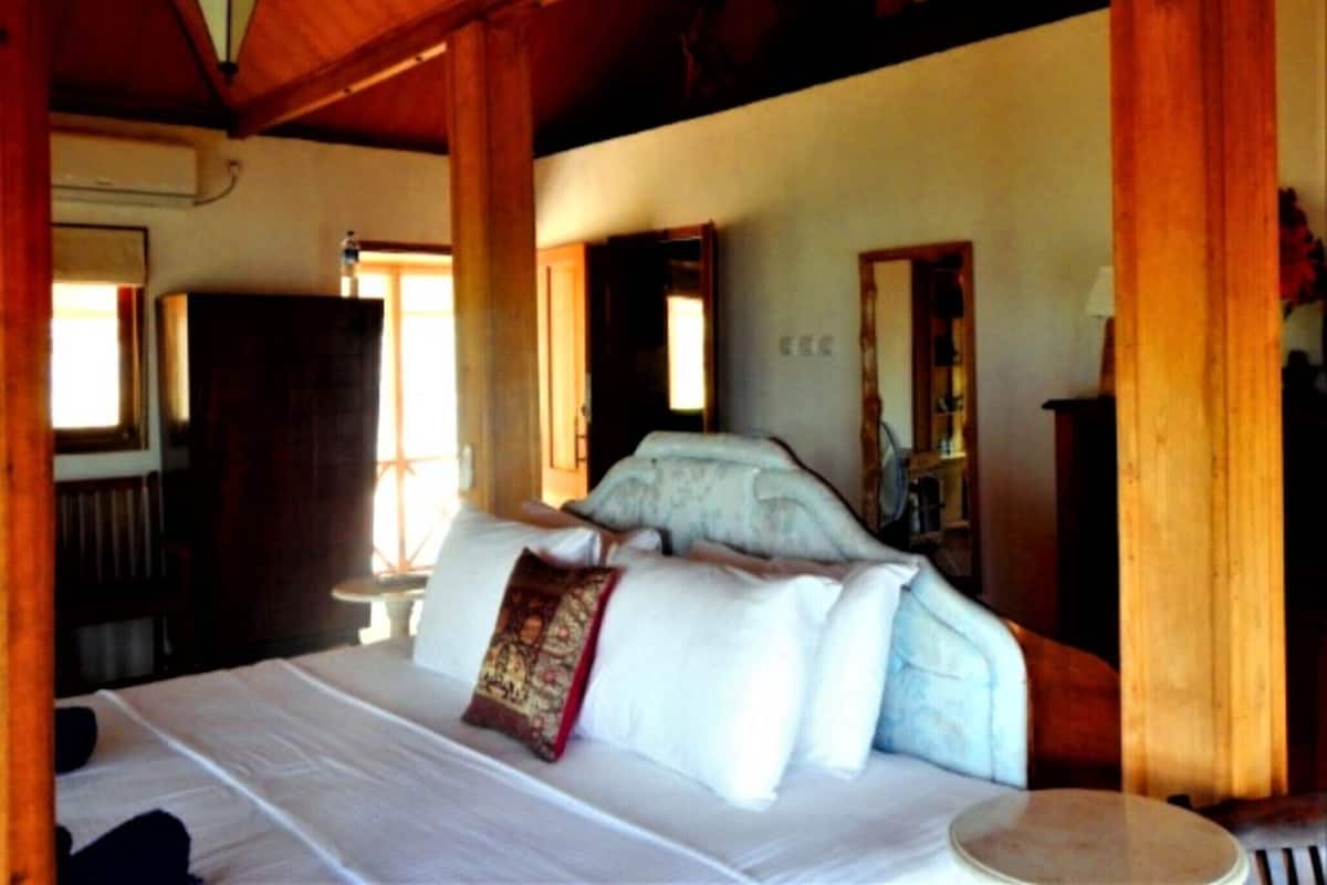 Una habitación con una cama, una mesa redonda, vigas de madera y una lámpara colgante.