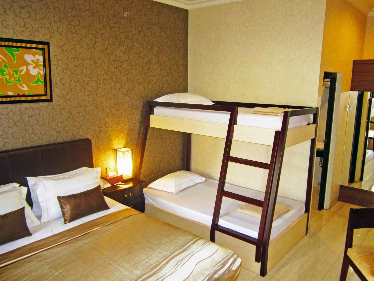 Een hotelkamer met een stapelbed, een nachtkastje met een lamp, een spiegel en een lijst met bloemenkunst aan de muur.