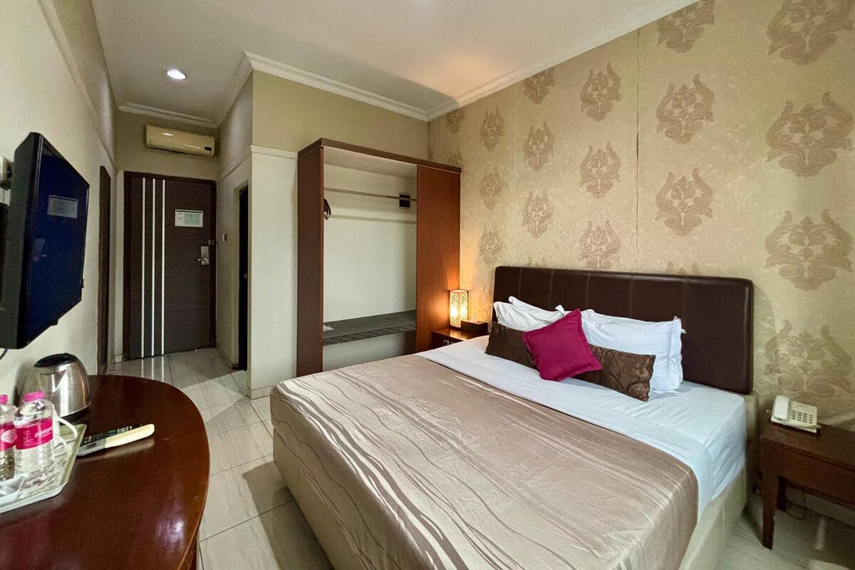 A hotel room with a large bed, a bedside table with a lamp, a telephone, and a wall-mounted TV.
