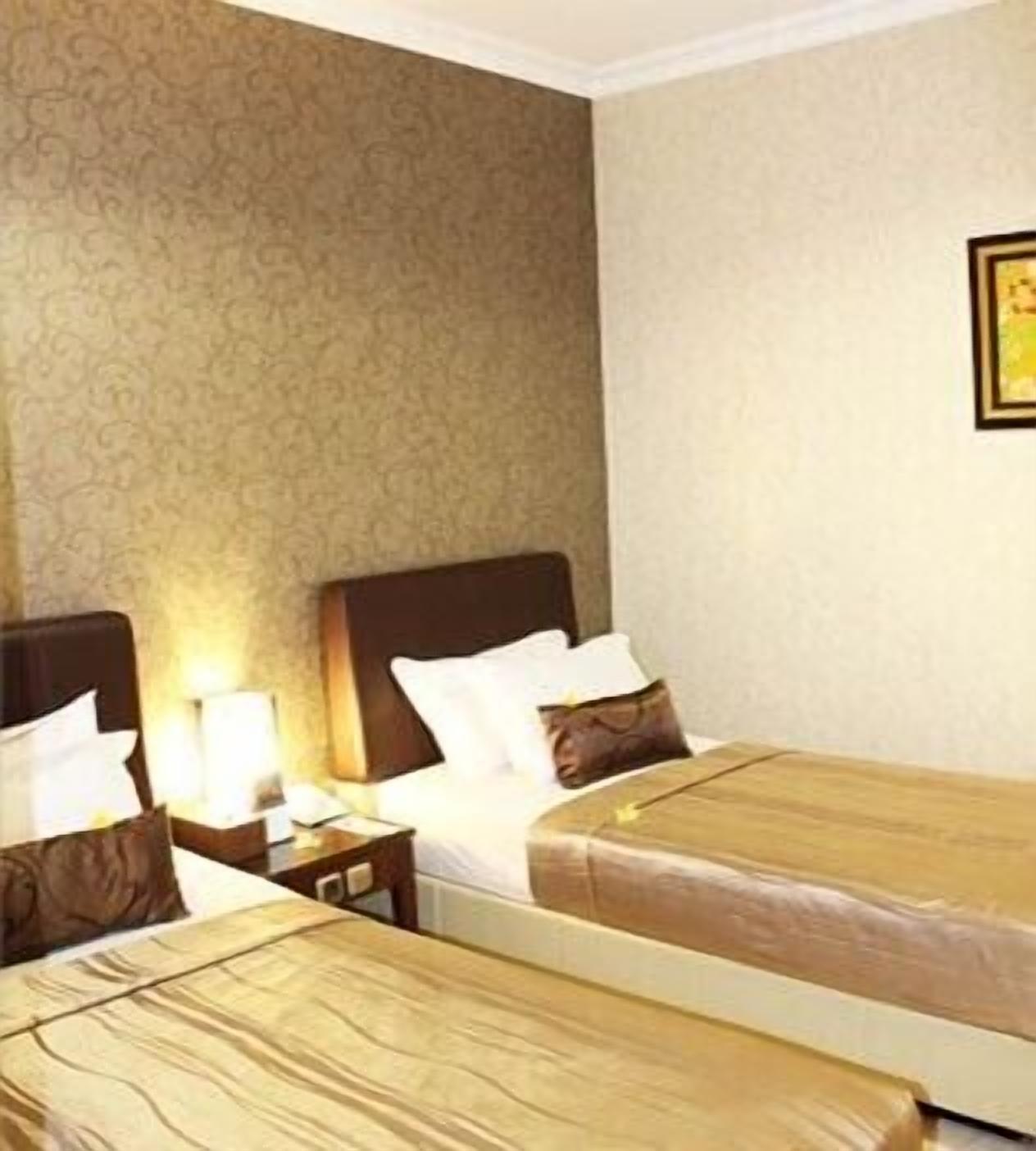 A hotel room with two single beds, a nightstand with a lamp, and a patterned wallpaper.