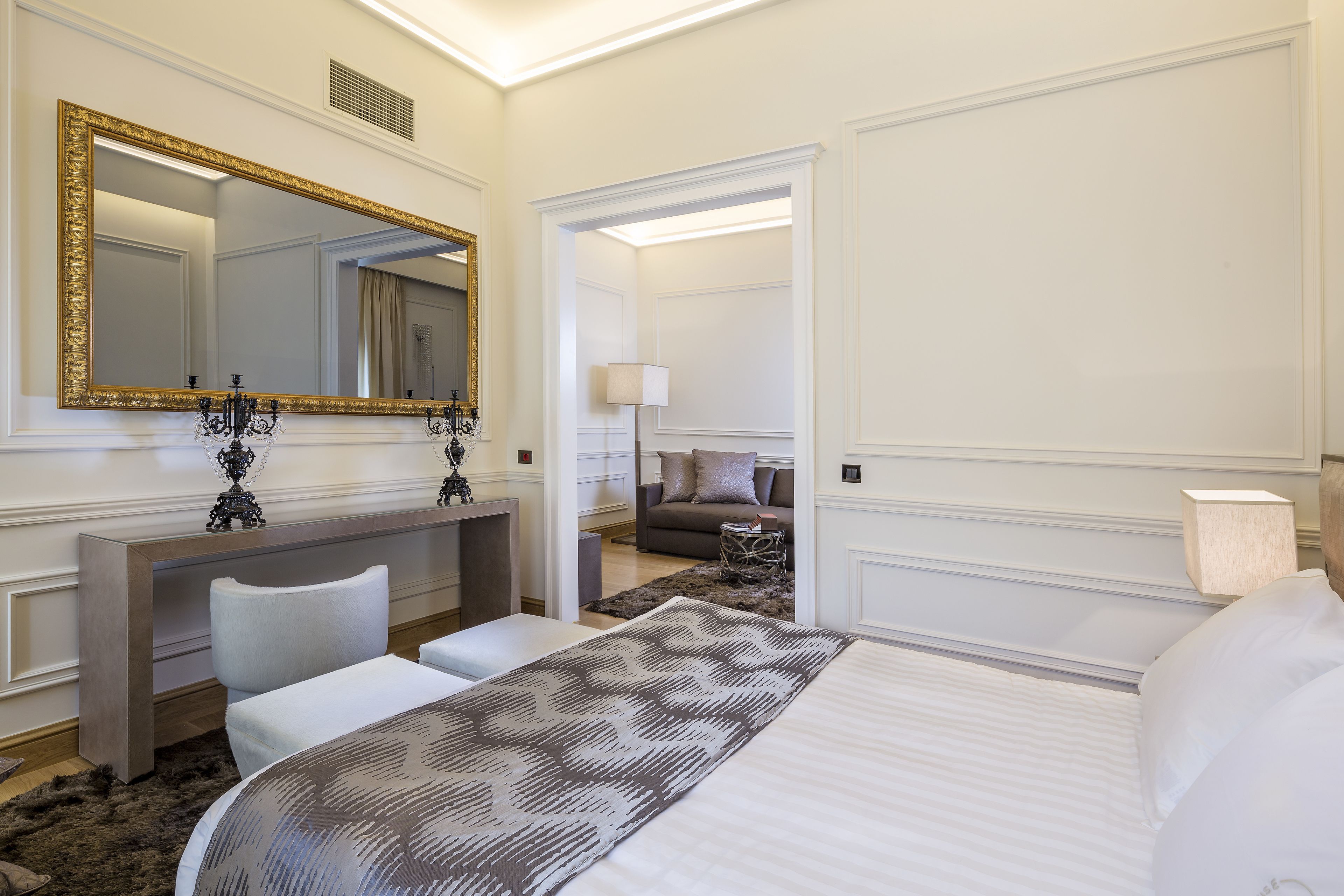 Una habitación de hotel con una cama grande, un tocador con espejo, un escritorio y un sofá al fondo.