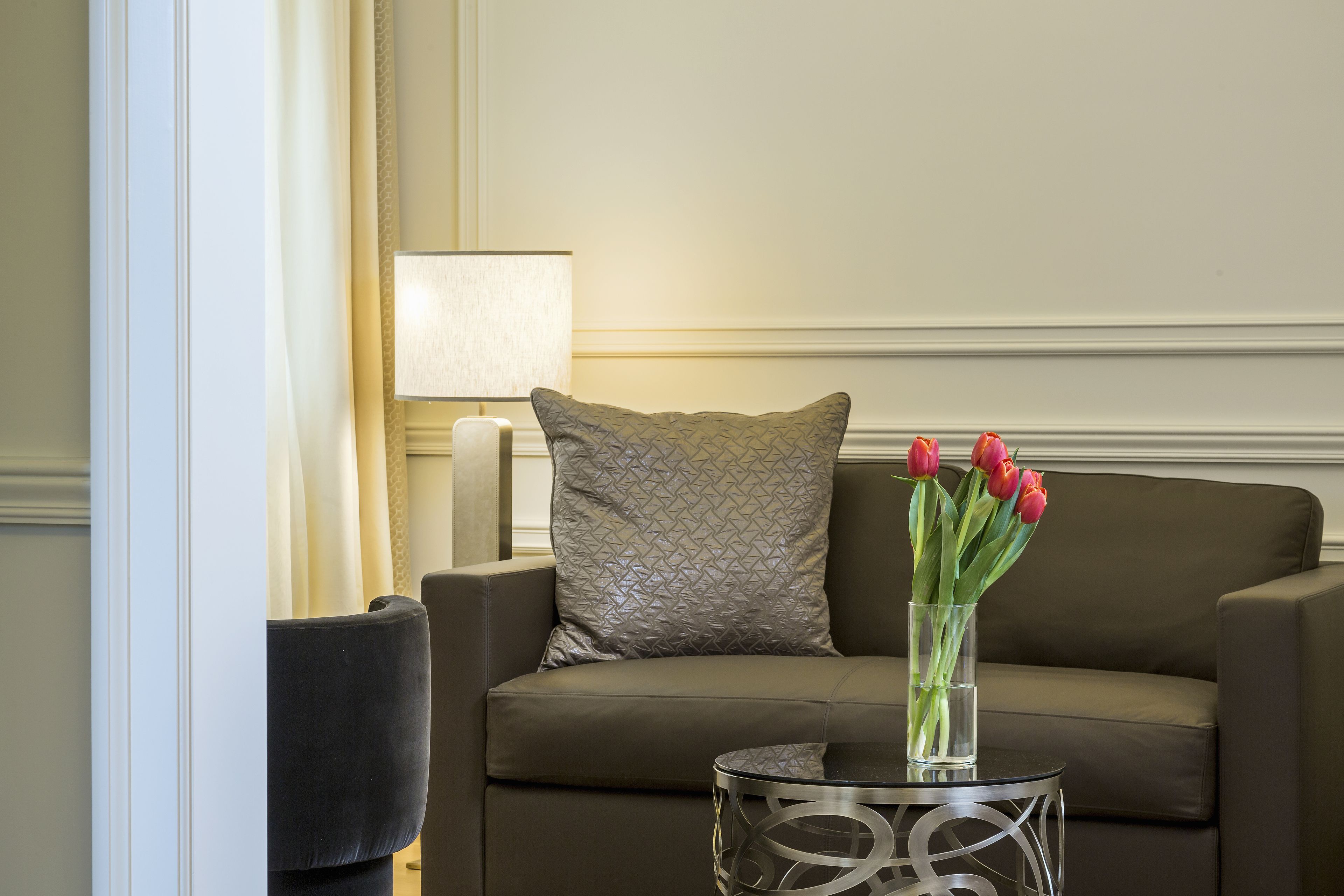 A modern living room with a sofa, a glass vase with red tulips, and a lamp.