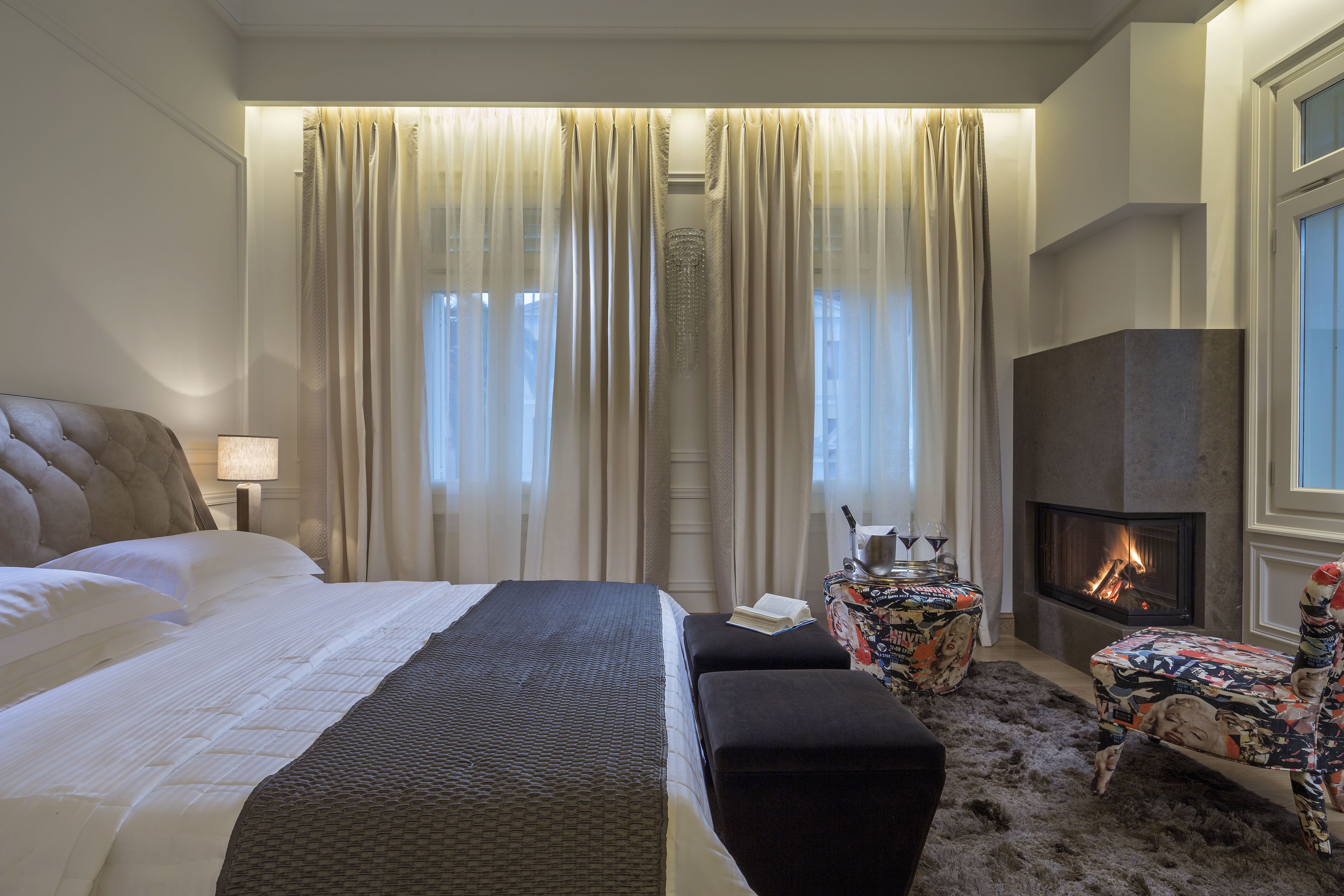 A hotel room with a large bed, a small sofa, a fireplace, and a decorative table.