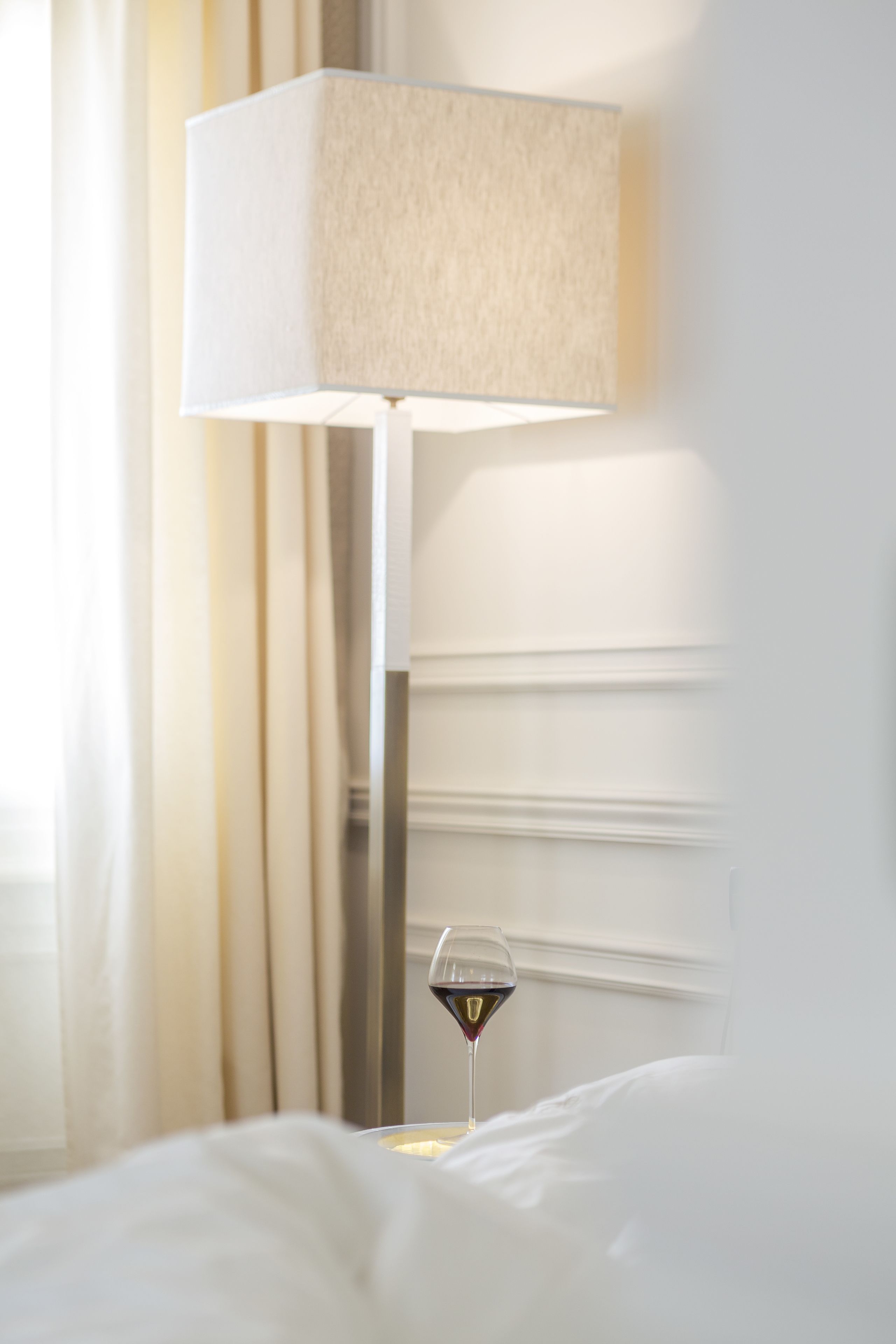 A bedside table with a glass of red wine and a lamp.