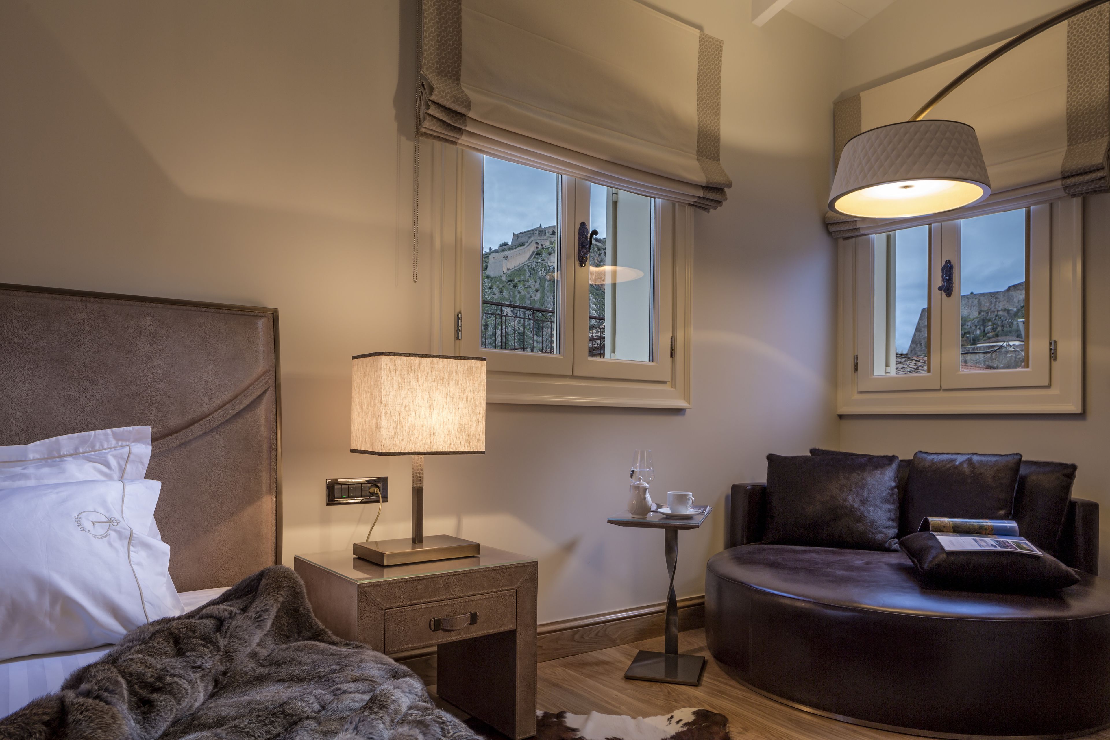 A bedroom with a bed, bedside table, lamp, and a view of a mountainous landscape through the window.