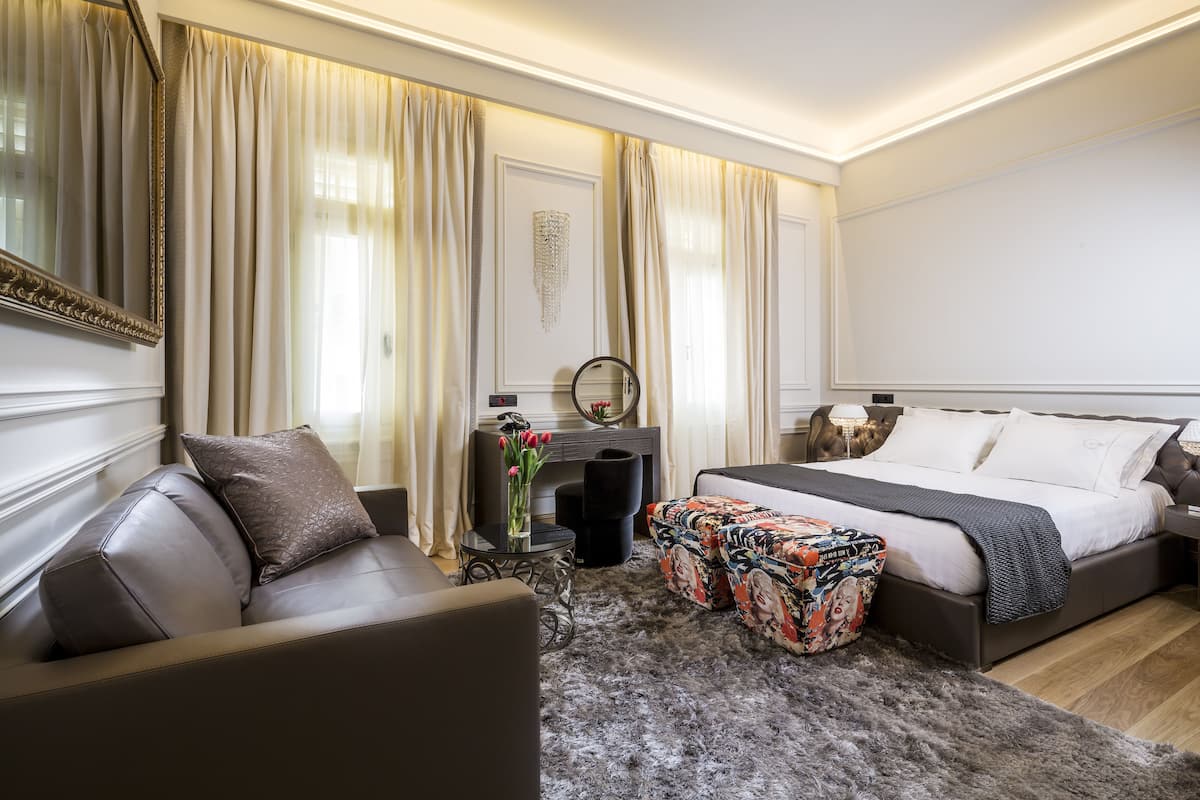 Une chambre d’hôtel avec un lit, un canapé, une petite table sur laquelle est posé un vase de fleurs et un miroir au mur.