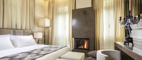 A hotel room with a large bed, a fireplace, a seating area, and a desk with a lamp.