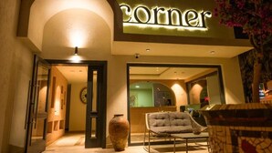 A hotel entrance with a 'corner' sign, a large vase, and a cushioned chair outside. - The Corner Hotel (Bodrum)