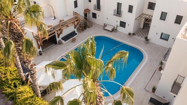 A rooftop pool area with palm trees, a wooden deck, and white buildings. - The Corner Hotel (Bodrum)