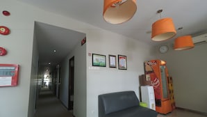 A lobby with a black leather sofa, orange pendant lights, framed awards, a clock, and a vending machine. - CityOne Xpress Semarang (Semarang)