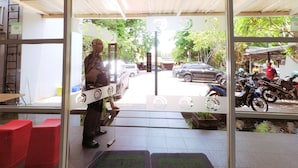 A view through a glass door of a building with a tiled floor, a person standing near a counter, and parked vehicles outside. - CityOne Xpress Semarang (Semarang)