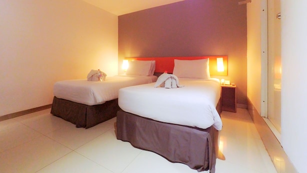 A hotel room with two beds, a nightstand, and a wall-mounted lamp. - CityOne Xpress Semarang (Semarang)