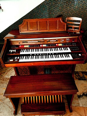 A grand piano with a wooden finish and a bench, placed in a room with patterned wallpaper. - Riad Dar Nador (Nador)