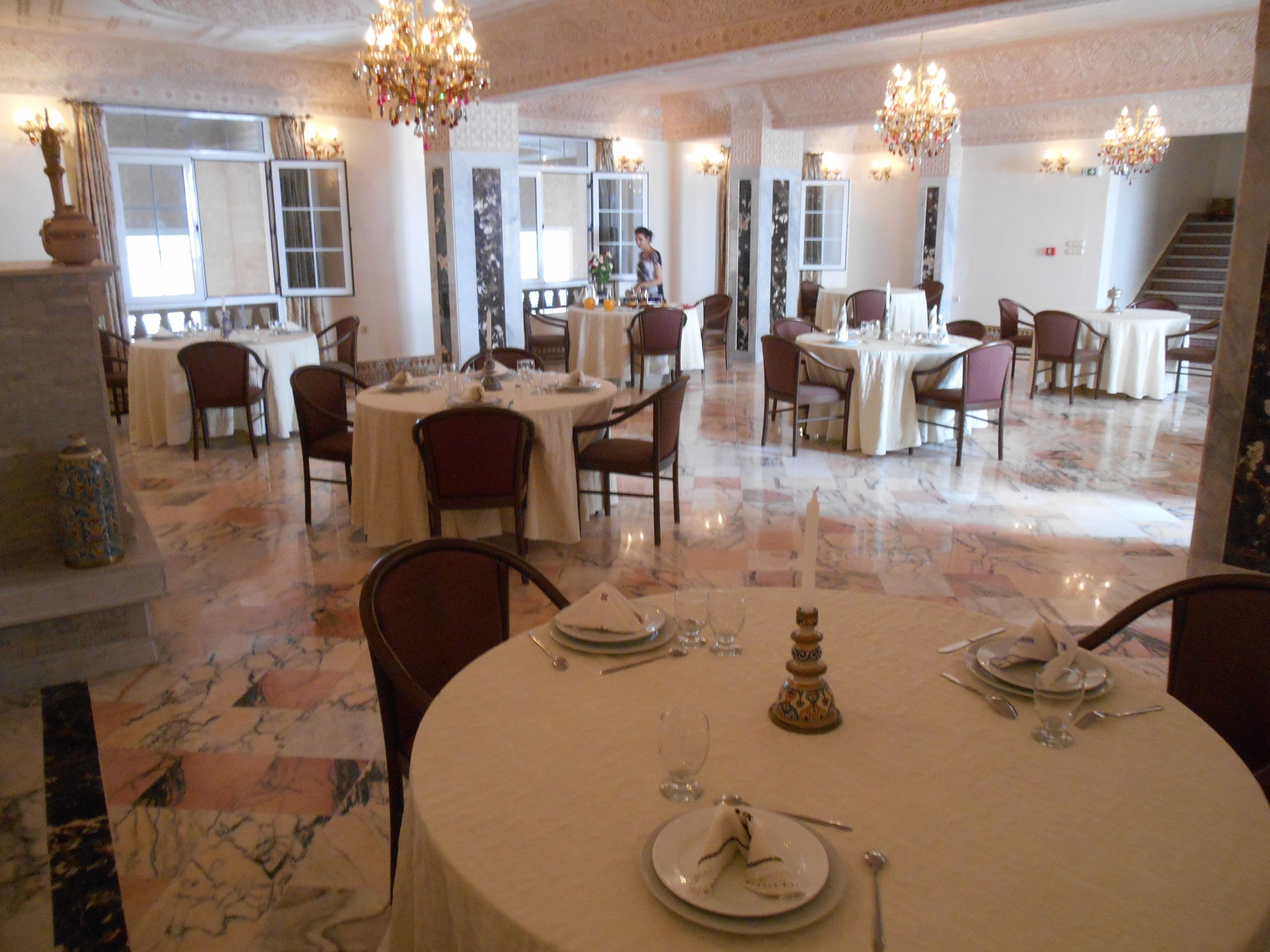 A spacious dining area with multiple round tables, each set with white tablecloths, chairs, and dining utensils.