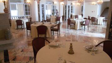 A spacious dining area with multiple round tables, each set with white tablecloths, chairs, and dining utensils.