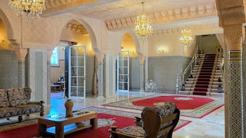 Un interior ornamentado con una gran escalera, candelabros y alfombras con diseños.