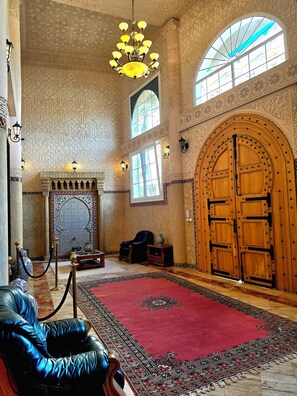 An interior with a large wooden door, a chandelier, and a patterned carpet. - Riad Dar Nador (Nador)