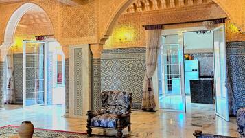 An ornate interior with a chandelier, patterned walls, and a red carpeted area.